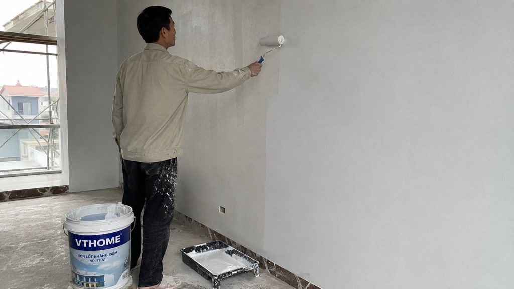 Thợ sơn VTHome dùng con lăn lăn lớp sơn lót lên tường trát phẳng đã bả, cạnh thùng sơn VTHome